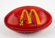 100th GAME FOOTBALL: A red Sherrin football with yellow McDonald’s logo, signed by Nathan Buckley and other players including Josh Mahoney, Brad Cassidy, Andrew Schauble, Jason Wild, Scott Russell, Simon Prestigiacomo, Paul Williams and others. Note: the - 3