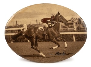 PHAR LAP: A small celluloid tin-plate oval depicting the classic image of jockey, Jim Pike riding Phar Lap at Flemington Racecourse, sometime in 1930. The sepia image has been carefully enhanced to reflect the correct colours of Pike's jacket. Overall 93 x 127mm. The only example known to us.