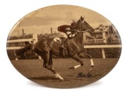 PHAR LAP: A small celluloid tin-plate oval depicting the classic image of jockey, Jim Pike riding Phar Lap at Flemington Racecourse, sometime in 1930. The sepia image has been carefully enhanced to reflect the correct colours of Pike's&nbsp; jacket. Overall 93