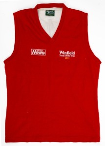 Northern Territory News ‘Team of the Year’ guernsey, 1991. Red sleeveless guernsey with yellow #2 on white patch on reverse. Presented to Nathan Buckley for being chosen in the newspaper’s Team of the Year. ‘Northern Territory News’ and ‘Winfield Team of the Year 1991’ badging on front. Unframed.