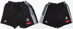 Nathan Buckley’s Collingwood training shorts, early 2000s. Adidas logo on right, Collingwood logo on left with Emirates patch below. Black shorts with grey panel with white stripes along edge. (2 pairs, different sizes).