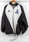 Collingwood players' jacket 1998. Adidas full-zip jacket with Collingwood logo on left breast above blue Primus patch. Mainly white front with black sleeves/sides and white stripes. Large white adidas logo on rear, above large white ‘Primus Telecommunicat