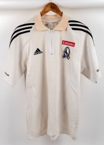 Collingwood players’ polo/top, circa 2006. White shirt with collar and half-zip, adidas logo on right breast, red Emirates on left above Collingwood logo. All white with black adidas stripes.