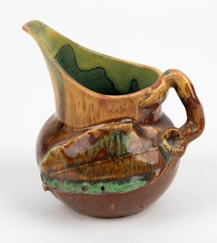 REMUED pottery jug with applied gumnut, leaf and branch handle, glazed in brown and green with pink highlights, incised "Remued", 10.5cm high