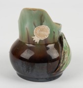 REMUED pottery jug with applied gumnuts, leaf and branch handle, glazed in brown and green with grey interior, incised "Remued, Hand Made", with original foil label, 10.5cm high - 3