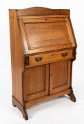 An antique Australian ash bureau with fiddleback paneled doors and bureau fall front, fitted interior with wool writing surface above a single drawer and cupboard base, circa 1920, 123cm high, 77cm wide, 40cm deep