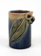 REMUED cylindrical pottery vase with applied gumnuts and leaf, glazed in blue and cream with pink highlights, incised "Remued, Hand Made", 10cm high