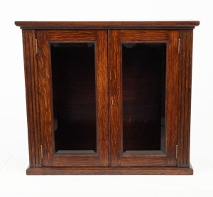 A solid English oak tabletop display cabinet with two bevelled glass panelled doors, fluted stiles and key, circa 1900, 53.5cm high, 60.5cm wide, 19cm deep