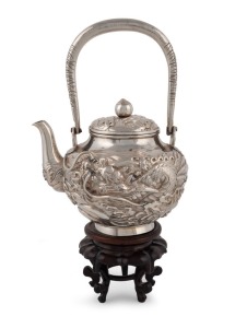 A Japanese export silver teapot with repousse dragon decoration, on carved timber stand, 19th/20th century, seal mark to base, the teapot 19cm high, 26cm high overall, silver weight 320 grams