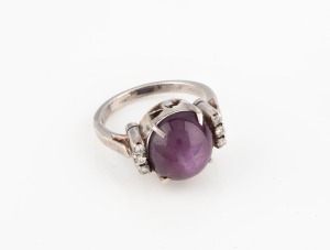 A vintage silver ring, set with a cabochon red star stone flanked by six brilliant cut white diamonds,