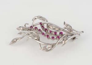 A vintage 18ct white gold foliate brooch, set with brilliant cut white diamonds and two rows of rubies, mid 20th century, 4.6cm wide, 7.1 grams
