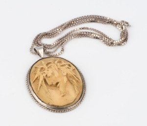 A vintage carved ivory pendant depicting Christ with crown of thorns, mounted in a sterling silver frame, suspended on a silver box-link chain, 20th century, the pendant 5.5cm high