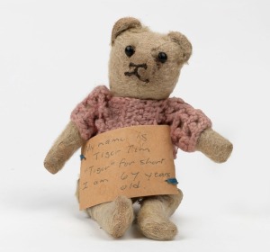 An antique English teddy bear with pink crochet top and affixed label "My name is Tiger Tim, Tiger for short. I am 67 years old.", circa 1915, 23cm high