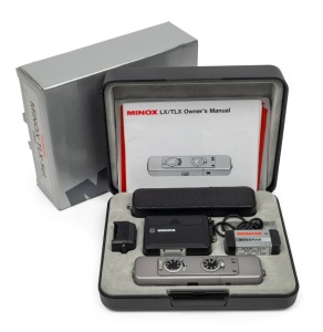 MINOX: Rare titanium-bodied Minox TLX subminiature camera [#2603313], c. 1995, with Minox 15mm f3.5 lens. Offered as a set in maker's case and outer box, with 8 x 11 flash accessory and adapter, Minopan film cartridge, black leatherette camera case, and c