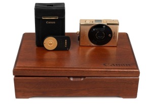 CANON: Limited-edition 18k gold-plated Elph compact camera [#000335], c. 1997, complete with velvet-lined wooden box, leather case, remote control, wrist strap, and printed matter. Issued to commemorate the 60th anniversary of the company.