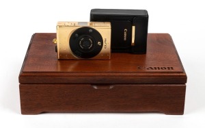 CANON: Limited-edition 18k gold-plated Elph compact camera [#000067], c. 1997, complete with velvet-lined wooden box, leather case, remote control, wrist strap, and printed matter. Issued to commemorate the 60th anniversary of the company.