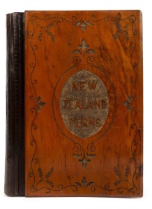 "NEW ZEALAND FERNS" by ERIC CRAIG, circa 1880. A stunning tome of pressed New Zealand fern specimens attractively displayed and captioned. Title page includes Maori cartes-de-visite portraits and lithograph view "SCENE IN TIKITAPU BUSH NEAR OHINEMUTU". Retailer's ink stamp "ERIC CRAIG, PRINCES ST. AUCKLAND". Finely carved mottle kauri boards with title and red morocco spine with gilt embossing. 19th century. Sheet size 44 x 31cm. (Folio)
