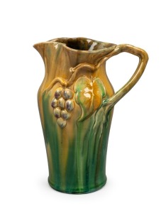 REMUED green and yellow glaze pottery jug with purple highlights, adored with applied grapes and leaf with branch handle, incised "Remued, Hand Made, 133", with original foil label, 25cm high