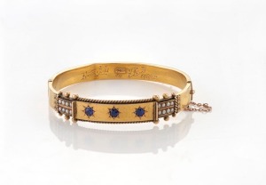 An antique Australian 15ct yellow gold bangle, set with three sapphires and seed pearls, housed in a F. BASSE & Co. VICE REGAL JEWELLERS, ADELAIDE, plush fitted box, 19th/20th century, stamped "R.15ct", 6cm wide, 14.2 grams