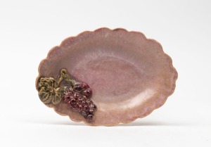 UNA DEERBON pink glazed pottery dish with applied grapes and leaf, signature obscured by glaze, ​​​​​​​19.5cm wide