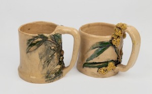 Two pottery mugs with applied wattle and eucalypt decoration, ​​​​​​​the larger 10cm high