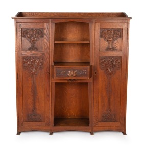 An Australian Arts & Crafts bookcase with knee hole desk compartment, manufactured in American oak, carved with Illawarra flame tree motif, early 20th century, with original ink stamp to the reverse of drawer "MISS GETHERS, WOOD CARVING STUDIO, SYDNEY", 168cm high, 152cm wide, 50cm deep