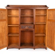 An Australian Arts & Crafts bookcase with knee hole desk compartment, manufactured in American oak, carved with Illawarra flame tree motif, early 20th century, with original ink stamp to the reverse of drawer "MISS GETHERS, WOOD CARVING STUDIO, SYDNEY", 1 - 6