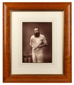 W.G. GRACE, posing in his cricket whites with a bat under his arm, the portrait by Herbert Rose Barraud, circa 1885; framed and glazed, overall 48 x 41cm.