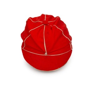 A TASMANIAN COLONIAL CRICKET CAP from the late 19th Century, red with white piping, a button-down peak, and with an illegible signature under the brim. Although worn in places, in remarkably good condition for one of the oldest surviving Australian cricket caps. Provenance: Charles Leski Auction, 30 September 2009.