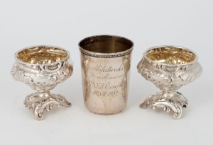 A Russian silver vodka beaker with inscription, together with a pair of French silver salt cellars in the Rococo style, (3 items), the beaker 5.8cm high, 100 grams total