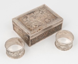 A pair of Asian silver napkin rings with bird and fan tree repouss&eacute; decoration and bamboo beaded edge, bearing character marks to the inside edge. Together with a Japanese style silver box with butterfly, chrysanthemum and bamboo decoration with Greek key