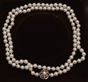 A cultured pearl necklace with an 18ct white gold, diamond and ruby clasp, 20th century, stamped "750, J.K.", the pearls approximately 6.5mm, 88cm long overall.