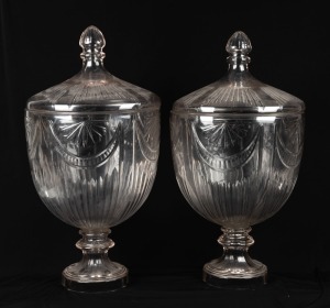 An impressive pair of vintage display cut glass bonbonnieres of classical urn form with pedestal bases and conforming lids with acorn style finials, 20th century, 66cm high, 37cm diameter.