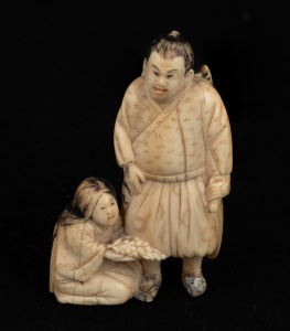 A Japanese carved ivory figural okimono of a standing man with kneeling woman, red seal mark to base, Meiji period, 19th/20th century, ​​​​​​​6cm high