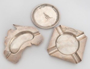 105 · A circular Australian silver dish engraved with a kangaroo, and two ash trays, one in the shape of the map of Australia, the other a souvenir of the Sydney Harbour Bridge, 20th century, (3 items). Makers include FAIRFAX & ROBERTS, and PROUD, the largest 11cm wide, 148 grams total.