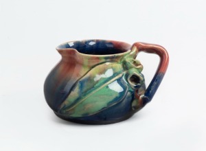 REMUED pottery jug with applied gumnuts, branch handle and leaf, glazed in pink, blue and green, incised "Remued, Hand Made, 173SM", 7cm high, 12cm wide