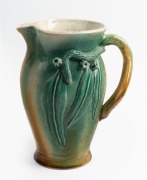 ARTIST UNKNOWN green and brown glazed pottery jug with applied gumnuts, leaves and branch handle in the Remued style, 26cm high
