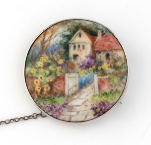 A silver mounted circular brooch with hand-painted porcelain cottage scene plaque, signed "SAUNDERS" on the reverse, 4cm diameter