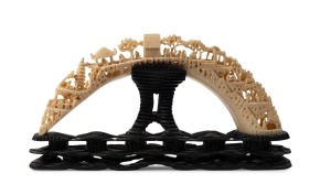 An antique Chinese carved hippopotamus tooth bridge on carved timber stand, 19th/20th century, ​​​​​​​18cm high, 34cm wide overall.