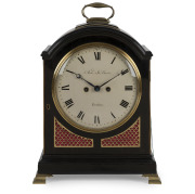 An antique English spring table clock in ebonized fruitwood case with brass bound single pad top and bail carrying handle, fish scale sound frets, standing on bracket feet. Original convex painted enamel dial with Roman numerals and maker's details "ARCH'