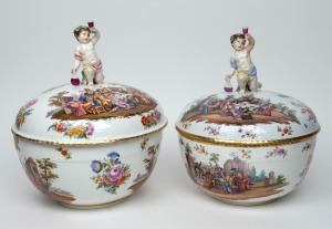 A graduated pair of ornate German hand-painted porcelain lidded tureens with Bacchanalian cupid finials, 19th/20th century, blue factory mark to base, 34cm and 33cm high