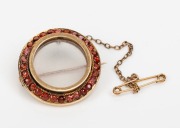 An antique 15ct gold circular brooch with garnet bezel and photo or mourning window, 19th century, ​​​​​​​2.5cm diameter, 7.8 grams including glass.