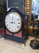 An antique English spring table clock in ebonized fruitwood case with brass bound single pad top and bail carrying handle, fish scale sound frets, standing on bracket feet. Original convex painted enamel dial with Roman numerals and maker's details "ARCH' - 2