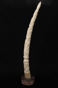 A carved marine ivory tusk ornament. most likely African origin, on carved wooden base, early to mid 20th century, 44cm high overall