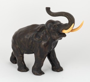 An antique cast spelter statue of an elephant with carved ivory tusks, early 20th century, stamped "Germany" to the underside of foot, 23cm high, 32cm long.