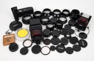 NIPPON KOGAKU: An accumulation of forty-two camera accessories, including one MD-15 motor drive, two Speedlight flash units, twenty-three lens caps, eleven lens hoods, four lens filters, and more. (42 items)