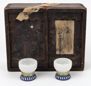 A pair of carved antique mutton jade cups on woven silk bases, housed in a blue silk lined timber box, 19th/20th century, the cups 3cm high, 5cm diameter, the case 23cm wide.