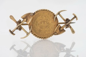 A South African gold miner's brooch set with an 1894 gold half pond coin, flanked by crossed picks and shovels, 5cm wide, 7.2 grams total.
