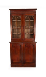 A Colonial Australian cedar two door bookcase in the Gothic style with adjustable shelves, astragal glazed upper doors and blind panel lower doors, Tasmanian origin, circa 1845, 250cm high, 100cm wide, 50cm deep.