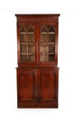 A Colonial Australian cedar two door bookcase in the Gothic style with adjustable shelves, astragal glazed upper doors and blind panel lower doors, Tasmanian origin, circa 1845, 250cm high, 100cm wide, 50cm deep.